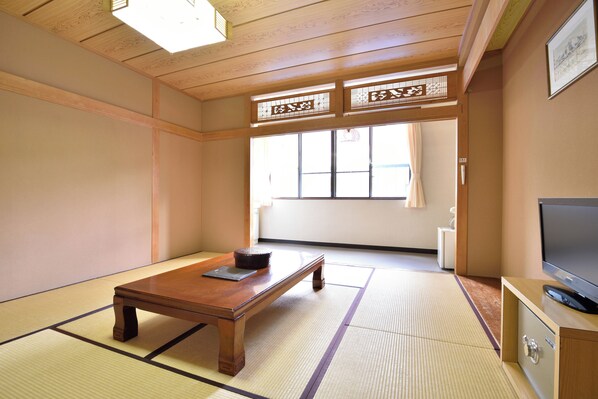 A traditional Japanese room with tatami flooring, a wooden table, a television on a cabinet, and a window with a view.