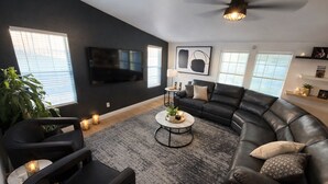 A modern living room with a sectional sofa, a flat-screen TV mounted on the wall, a coffee table with decorative items, and a large potted plant. - Red Rock Retreat (Page)