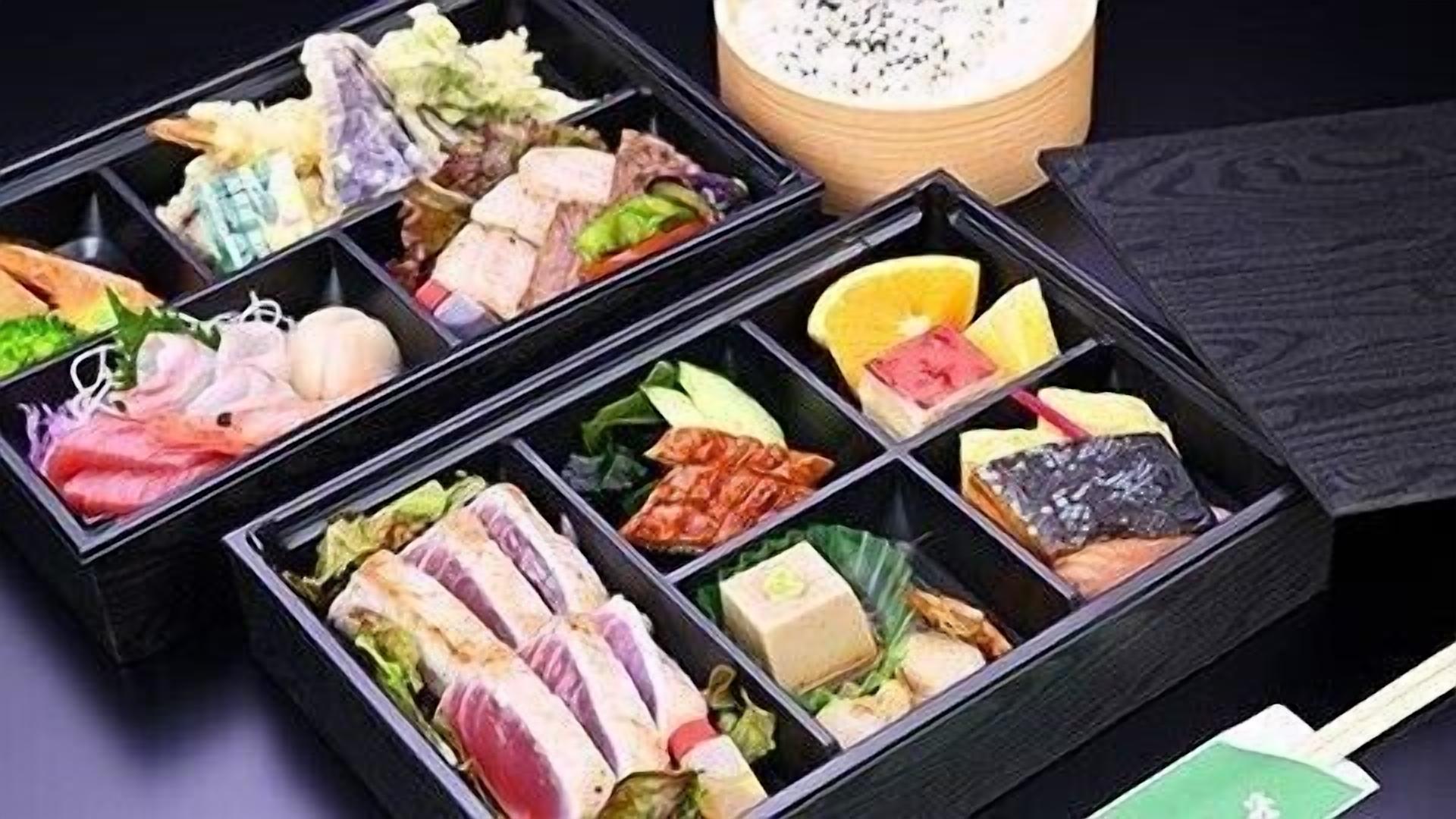 A bento box with various food items including fish, vegetables, and a small container of soup.