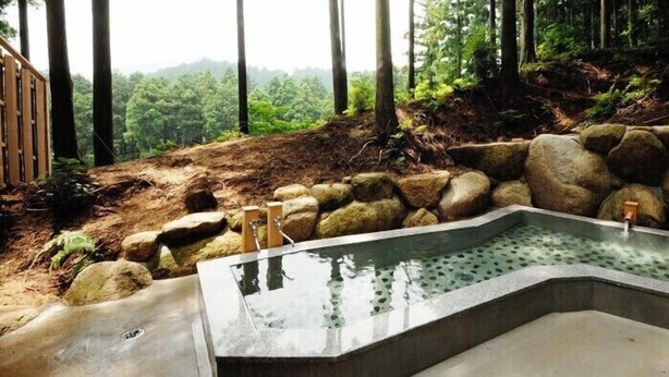 Un jacuzzi rodeado de rocas y árboles, con una terraza de madera y vistas a una ladera boscosa.