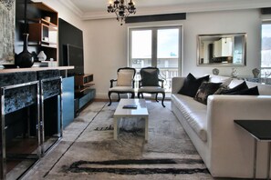 Un salon moderne avec un canapé blanc, deux fauteuils, une table basse et une grande fenêtre donnant sur un paysage.