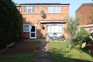 A two-story brick house with a satellite dish, a small garden with a pathway, and a patio with outdoor furniture. - Skyvillion - Valley Way - 3Bed House in Stevenage (Shephall)