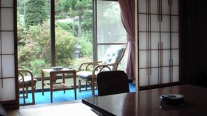 Una habitación con suelo de tatami, una mesita baja y vistas a un jardín a través de amplias ventanas.