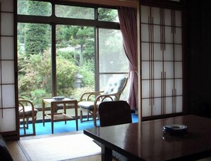 A room with tatami flooring, a low table, and a view of a garden through large windows.