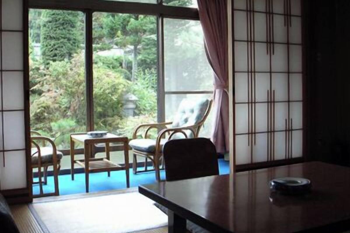 Una habitación con suelo de tatami, una mesita baja y vistas a un jardín a través de amplias ventanas.