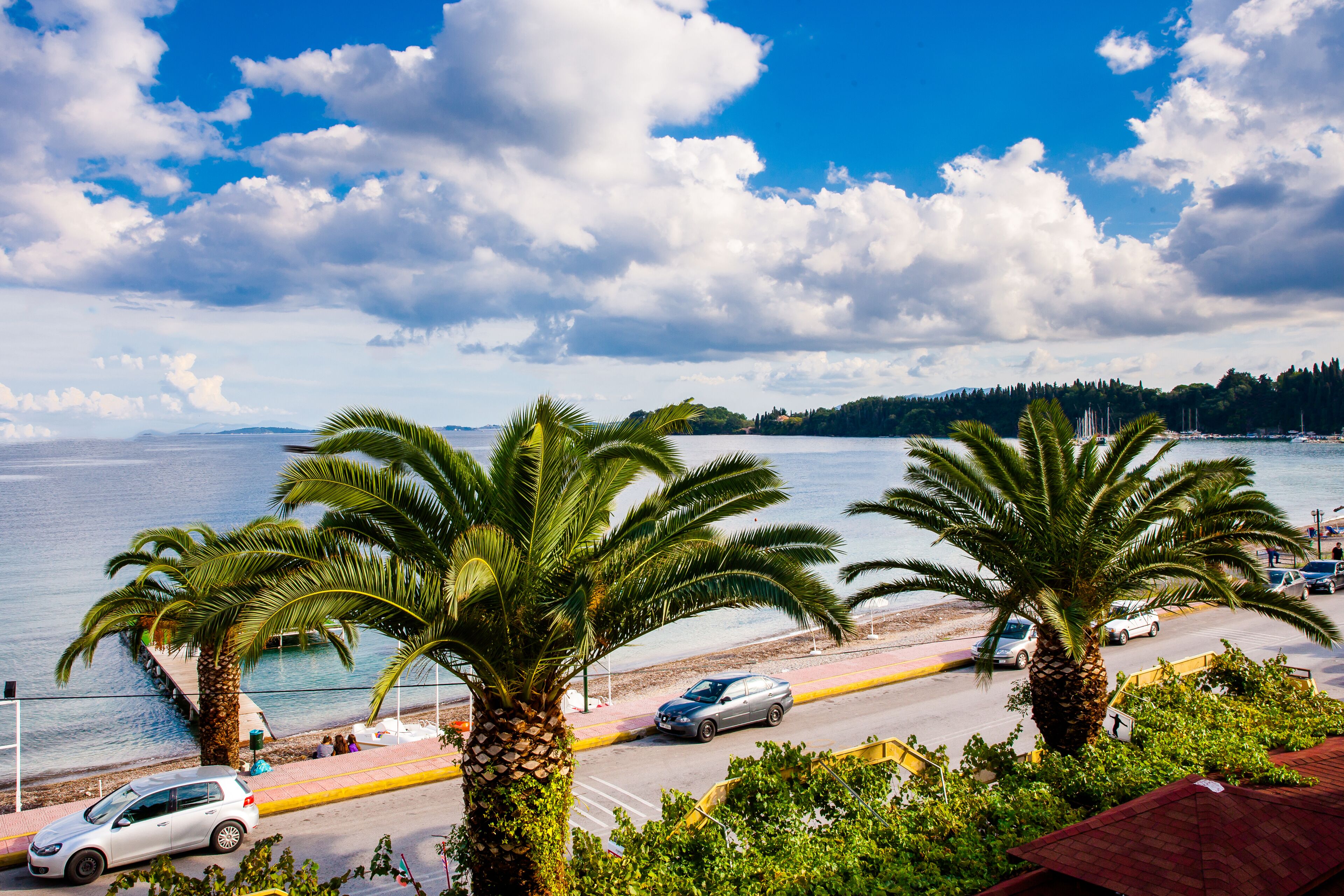 Una carretera costera con palmeras, una playa y cielo despejado.
