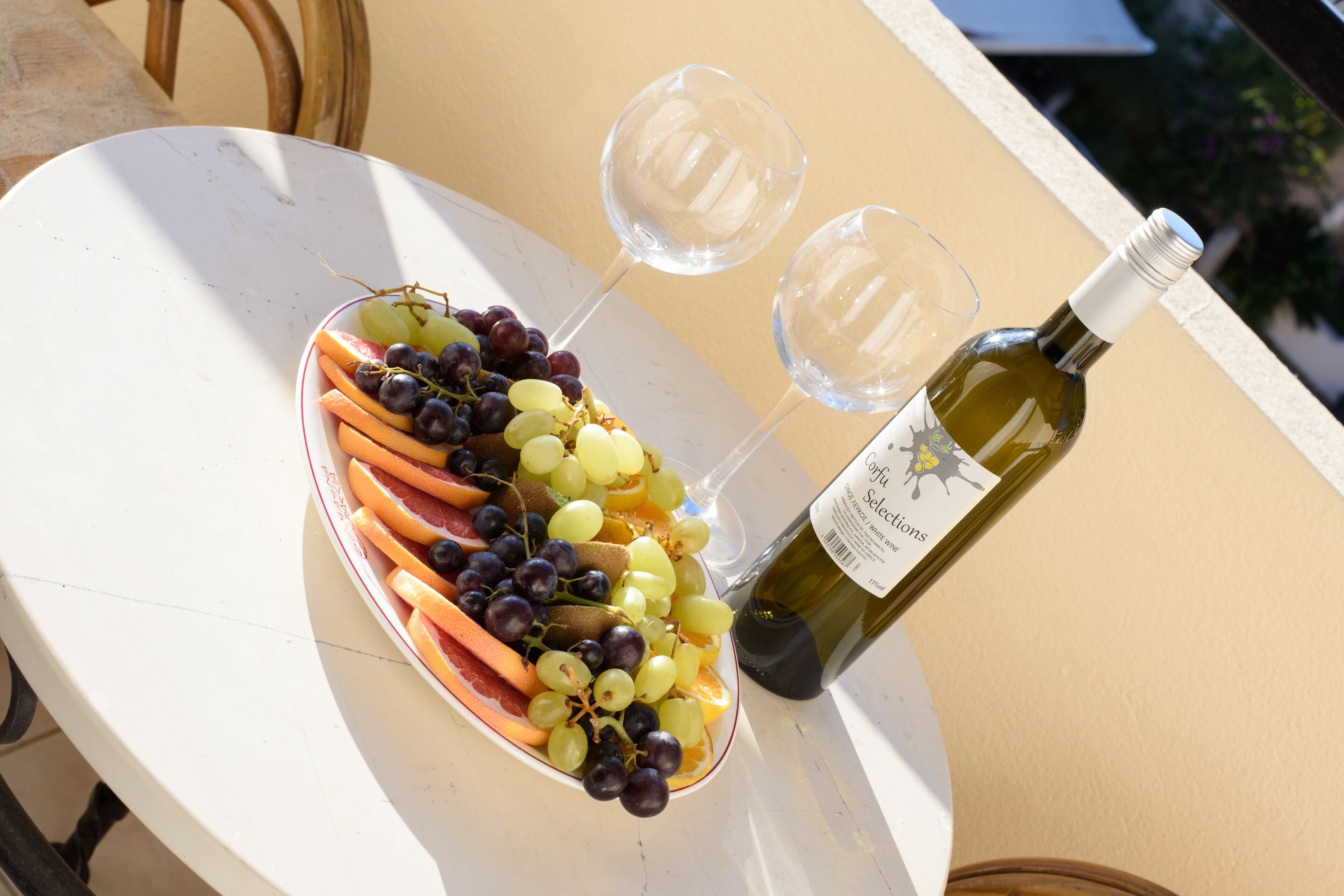 Une table avec un plateau de fruits, deux verres à vin et une bouteille de vin.