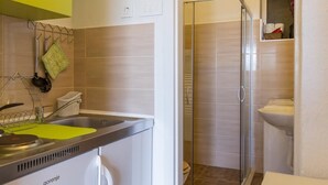 Eine kompakte Küche mit integriertem Geschirrspüler, einem kleinen Spülbecken und einem leuchtend gelben Schrank.