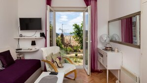 Ein Zimmer mit einem Bett, einem Sessel, einem Fernseher, einem Schreibtisch und Blick ins Freie.