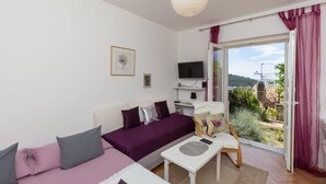 Ein modernes Wohnzimmer mit einer Couch, einem Couchtisch und einem Fernseher. Ein Balkon bietet Blick ins Grüne.