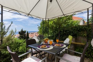 An outdoor dining area with a table set for two, overlooking a scenic view of a coastal town.