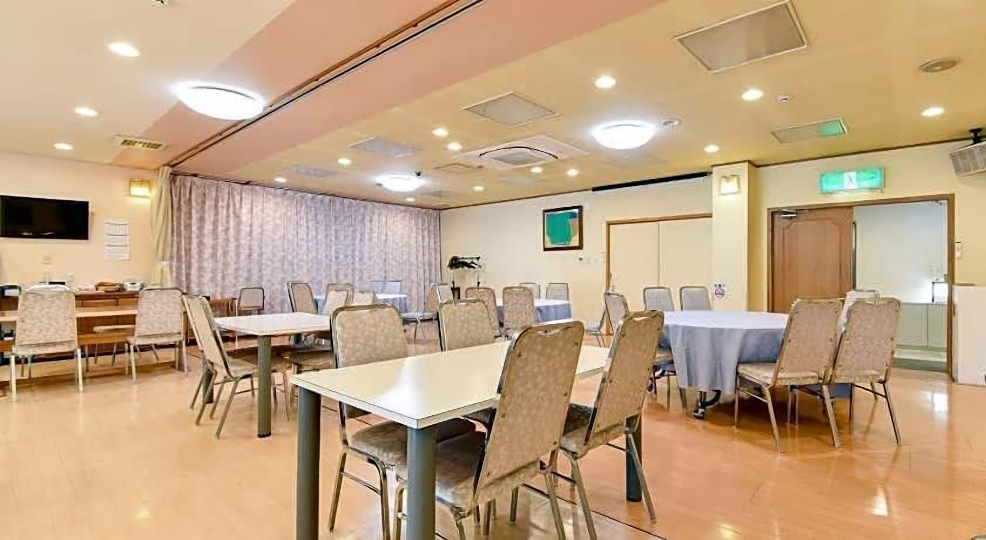A conference room with tables and chairs, a television, and a door with an emergency exit sign.