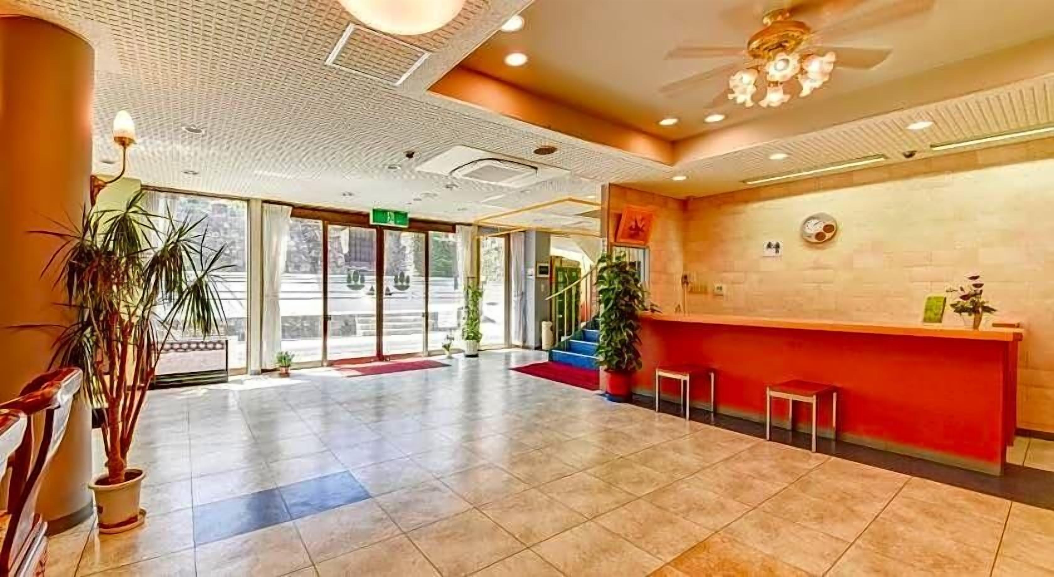 A hotel reception area with a red counter, a waiting area, and a large window.