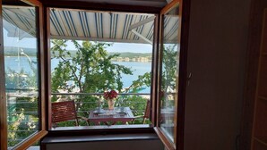 Ein Balkon mit Tisch und Stühlen, einer Blumenvase und Blick auf einen See und Gebäude.
