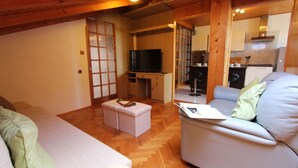 Ein gemütliches Wohnzimmer mit einer Couch, Hocker und einem Fernseher auf einem Holzständer.