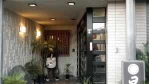 A building entrance with a tiled wall, potted plants, and a wooden door. - Hinode Ryokan (Fukui)