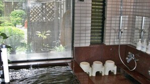 A bathroom with a bathtub, shower, and toilet. There is a window with a view of greenery outside. - Hinode Ryokan (Fukui)