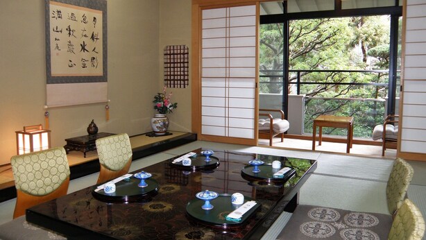 A traditional Japanese room with tatami flooring, a low table with tea sets, a shoji screen, and a view of trees through a sliding door. - Hinode Ryokan (Fukui)