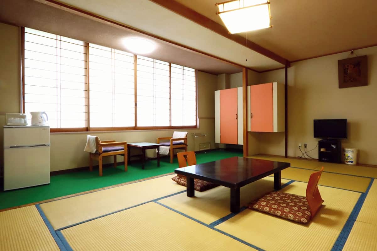 Une pièce avec un sol recouvert de tatamis, comprenant une table en tatami, des chaises, un téléviseur et un réfrigérateur.