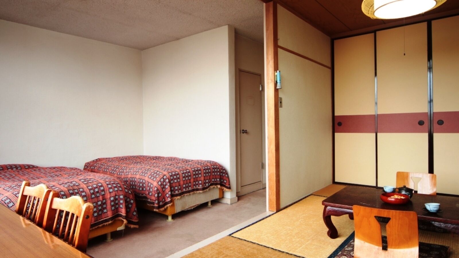 A traditional Japanese room with tatami flooring, two beds with patterned bedding, a wooden table with a bowl, and sliding doors.