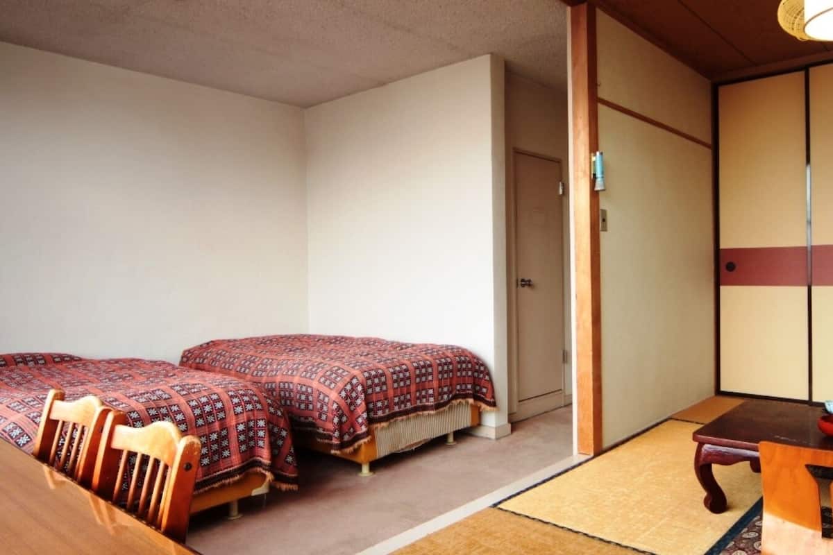 A traditional Japanese room with tatami flooring, two beds with patterned bedding, a wooden table with a bowl, and sliding doors.