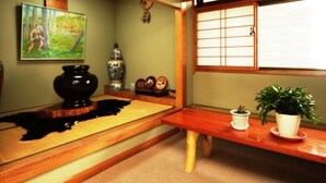 A traditional Japanese room with tatami flooring, a shoji screen, a black ceramic bowl, a ceramic vase, and a potted plant. - Shikanoyu Tsuchiya (Tsumagoi)