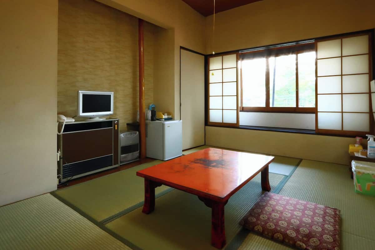 Une pièce de style japonais traditionnel, avec un sol recouvert de tatamis, une table basse, un téléviseur, un réfrigérateur et une fenêtre dotée de panneaux coulissants en papier de riz (shoji).