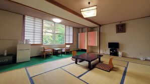 A traditional Japanese room with tatami flooring, a low table, chairs, a refrigerator, and a television. - Shikanoyu Tsuchiya (Tsumagoi)