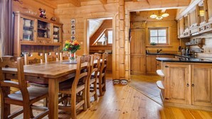 Interior de una cabaña de madera con comedor, cocina y una escalera que lleva a un nivel superior.