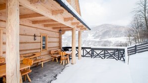 Una cabaña de madera con un porche cubierto, bancos de madera y vistas a montañas nevadas.