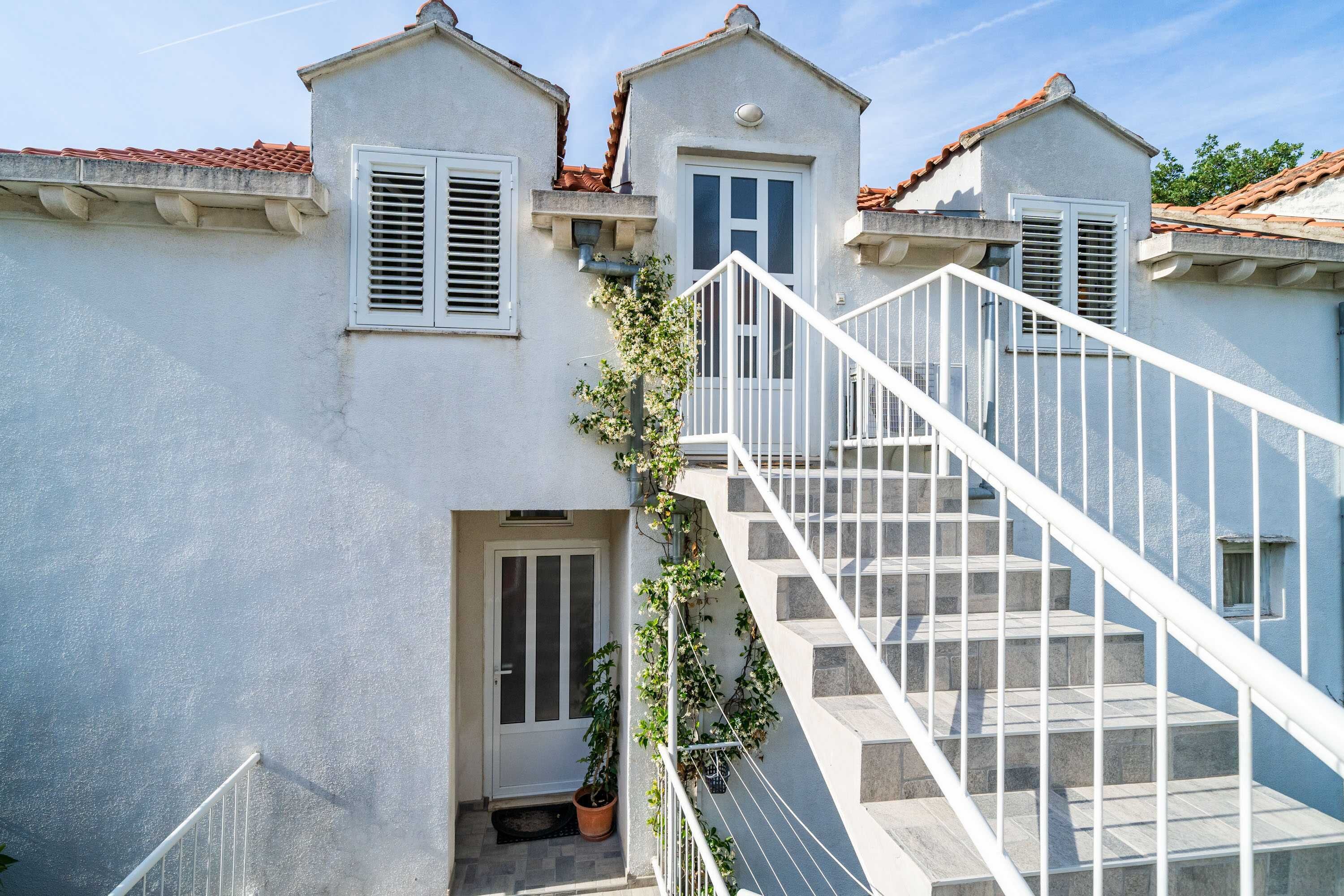 Un bâtiment à deux étages, avec une façade blanche, un toit recouvert de tuiles et un escalier blanc doté de rampes.