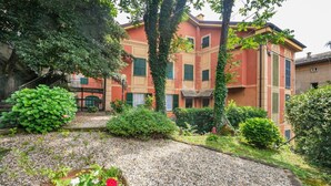 Un patio con un sendero de grava, una planta en maceta con flores, y un edificio con persianas verdes y fachada roja.