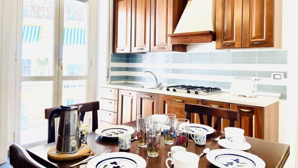 A kitchen with wooden cabinets, a gas stove, and a dining table set with plates, cups, and glasses. - CASA di Ale & Frank (Salerno)