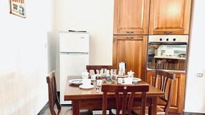 A kitchen with wooden cabinets, a white refrigerator, and a dining table set with cups and glasses. - CASA di Ale & Frank (Salerno)