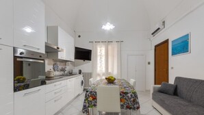 A compact kitchen with white cabinets, a built-in oven, and a dining area with a table set for four. - Dimora del Delfino Curioso (Lecce)