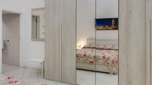 A bedroom with a bed, a nightstand, a chair, a mirror, and a wall-mounted light fixture. - Dimora del Delfino Curioso (Lecce)