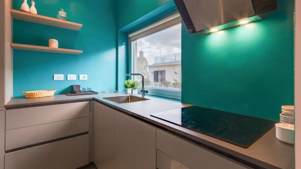 A modern kitchen with teal walls, a window, and a stainless steel range hood. - Inner City Apartments (Lecce)