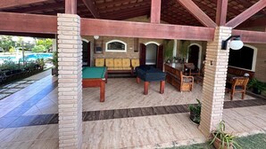 A covered outdoor area with a pool table, sofas, and a brick pillar. - Country house in Atibaia for rent with swimming pool with solar heating and Wi-Fi. (Atibaia)