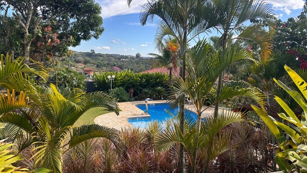 A pool surrounded by lush tropical plants and a view of a hilly landscape. - Country house in Atibaia for rent with swimming pool with solar heating and Wi-Fi. (Atibaia)