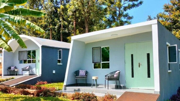Ein modernes, zweistöckiges Haus mit flachem Dach, großen Fenstern und einer kleinen Veranda.