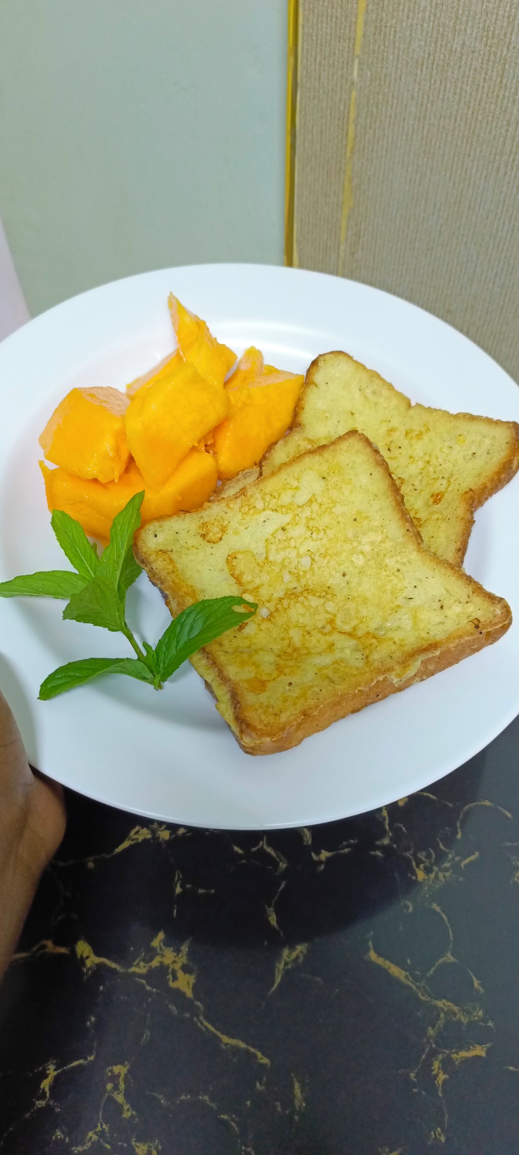 Ein Teller mit Toast und Mangostücken, garniert mit Minzblättern.
