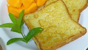 Een bord met toast en stukjes mango, versierd met muntblaadjes.