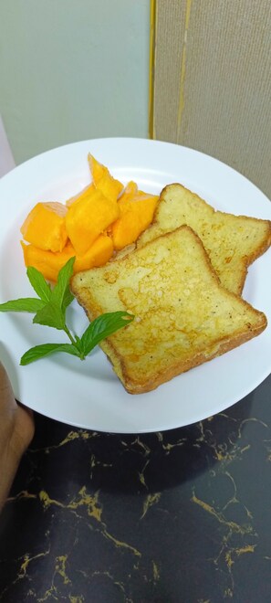 Een bord met toast en stukjes mango, versierd met muntblaadjes.