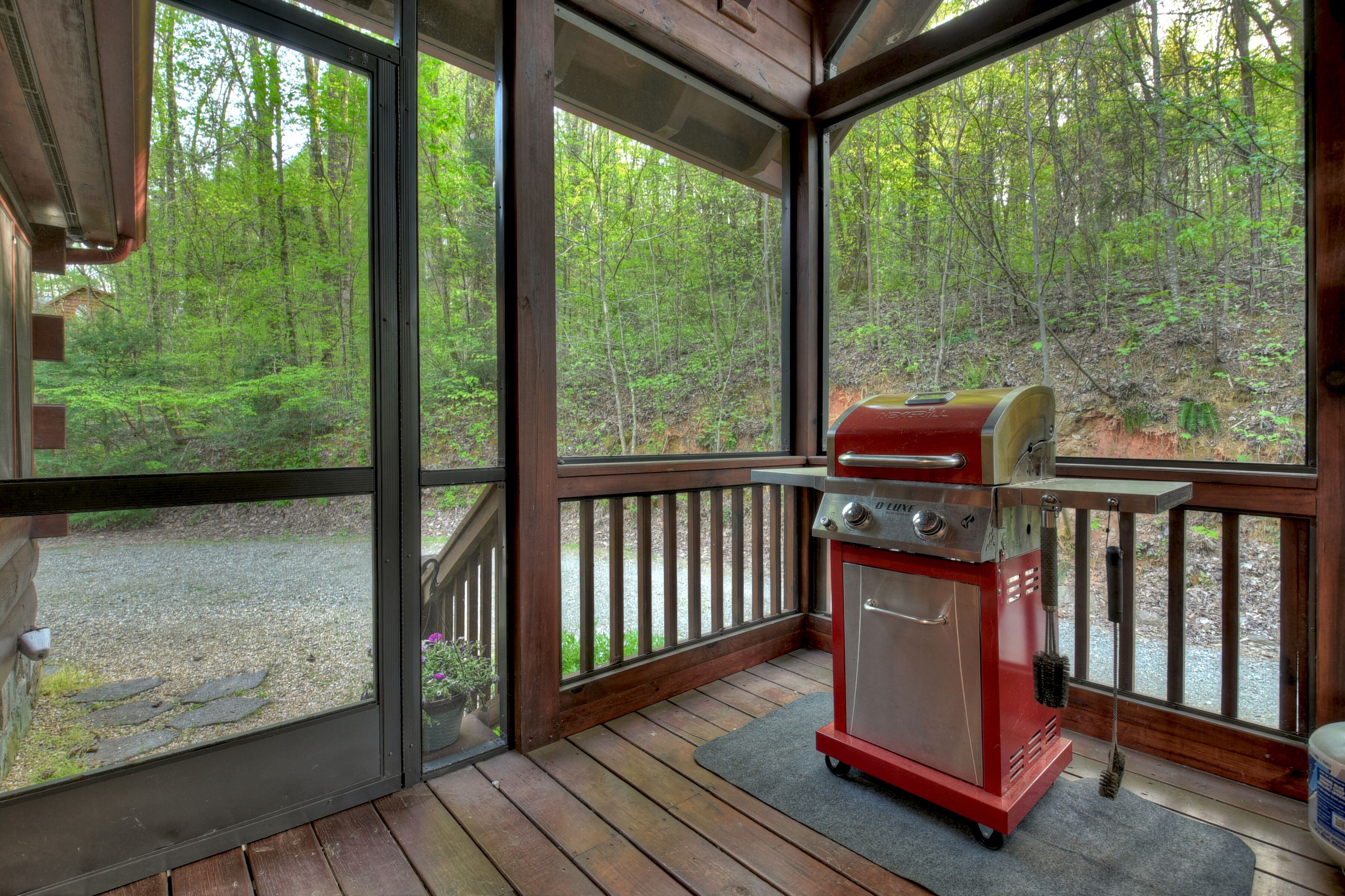 A covered outdoor area with a grill and a view of a forest.