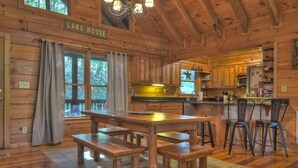 A wooden cabin interior with a dining table, benches, and a kitchen area. - Lakeside Cabin w/ mountain views, dock, fire pit, hot tub, and much more! (Ellijay)