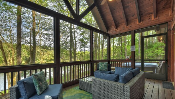 A covered outdoor seating area with wicker furniture and a view of a forested area. - Lakeside Cabin w/ mountain views, dock, fire pit, hot tub, and much more! (Ellijay)