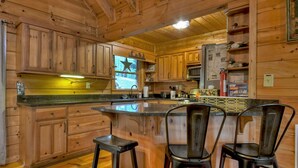 A wooden cabin kitchen with a bar area, wooden cabinets, and two bar stools. - Lakeside Cabin w/ mountain views, dock, fire pit, hot tub, and much more! (Ellijay)