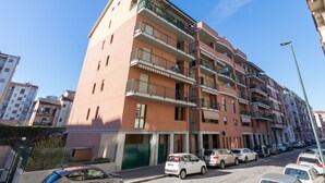 Un immeuble résidentiel à plusieurs étages, doté de balcons, avec des voitures garées et un ciel dégagé.