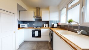 Een kleine keuken met witte kasten, een magnetron, een fornuis, een oven en een vaatwasser.