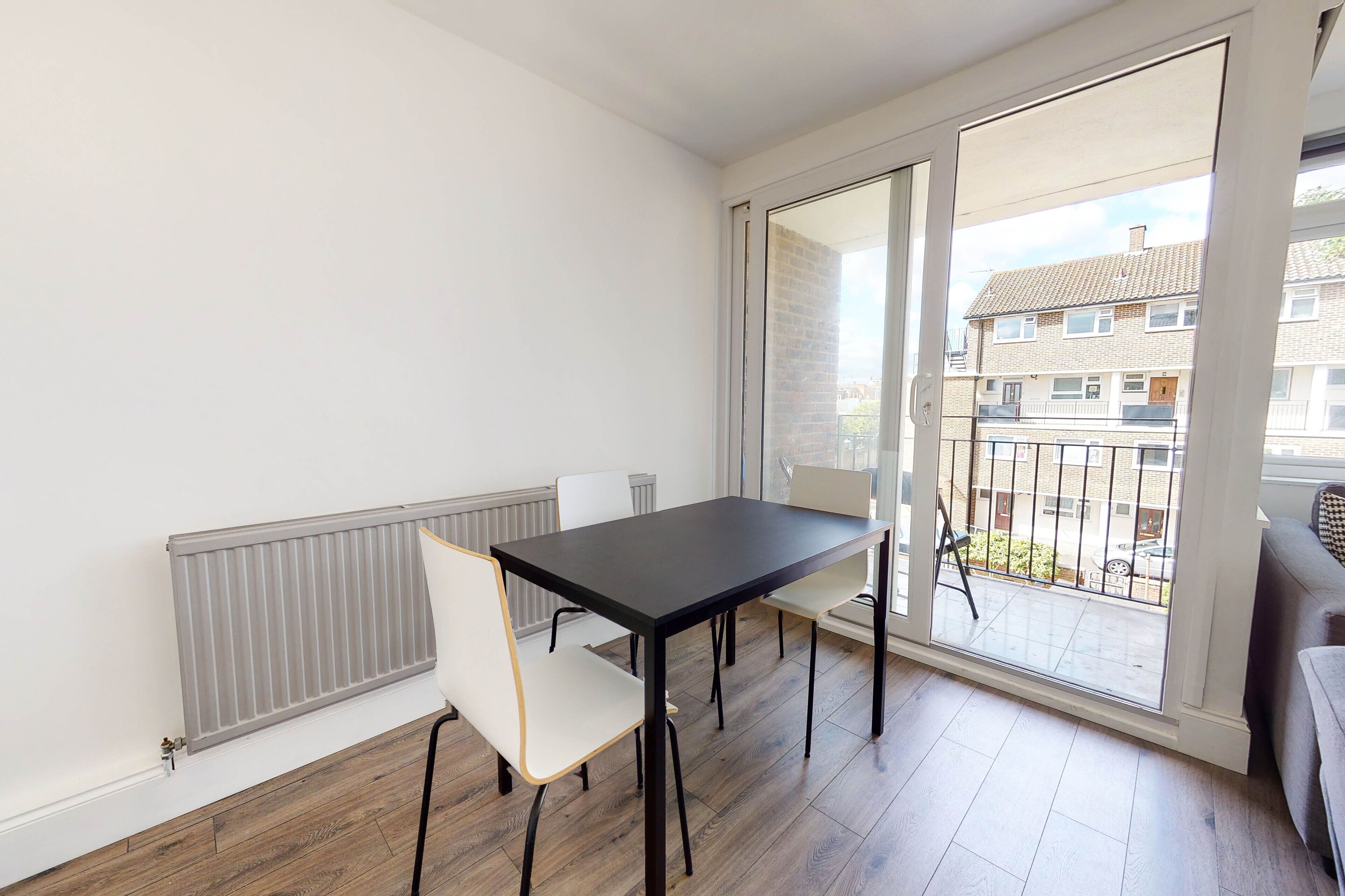 Varanda com mesa e cadeiras, um radiador e vista para edifícios vizinhos.